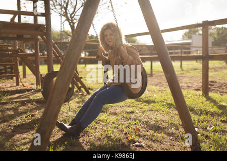 Porträt der glückliche junge Frau Wintermantel schwingen in Spielplatz Stockfoto