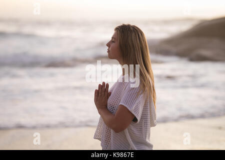Seitenansicht der jungen Frau Meditation am Strand bei Sonnenuntergang Stockfoto