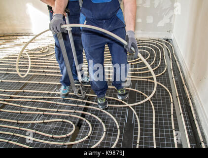 Handwerker bei der Verlegung von Rohrleitungen der Fußbodenheizung Stockfoto