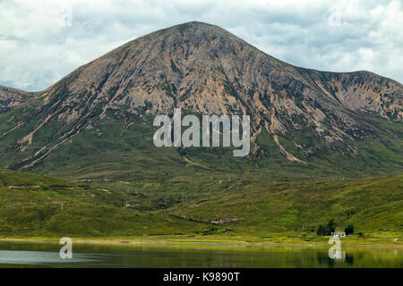 Ein kleines Haus mit Glamaig Berg auf der Isle of Skye und Loch Ainort im Vordergrund. Stockfoto