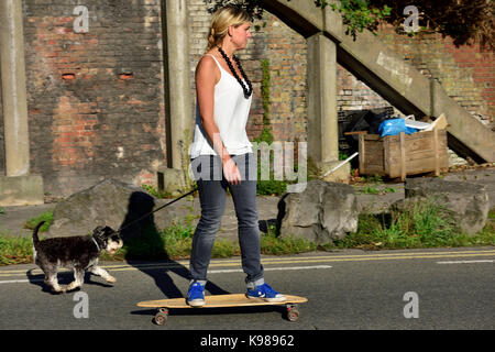 Frau auf Skateboard mit Hund für einen Spaziergang Stockfoto