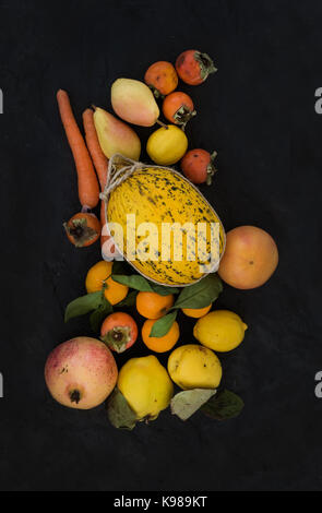 Gelb orange Obst und Gemüse Sortiment gemischt, Zutaten für Smoothie. Melone, Granat, Grapefruit, Karotte, Kaki, Zitrone, Quitte, Birne über schwarzen Schiefer Hintergrund Stockfoto
