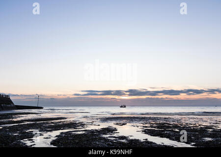 England, Broadstairs. Viking Bay mit den Sonnenaufgang über dem Meer. Im Vordergrund ist das Meer, Algen und Sand. Tide ist out. Fischerboot in Mitte, am Horizont. Stockfoto