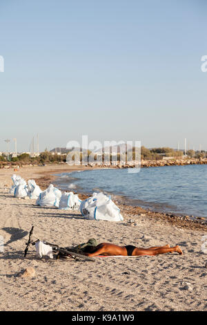 Ein Mann ist Sonnenbaden am Strand von Glyfada (Athen, Griechenland), die durch die Ölpest verunreinigt ist. Die weißen Beutel neben dem Mann sind voll von Rohöl. Stockfoto