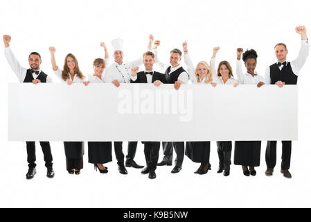 Portrait von glücklichen Angestellten im Restaurant mit erhobenen Armen halten leere Plakatwand vor weißem Hintergrund Stockfoto