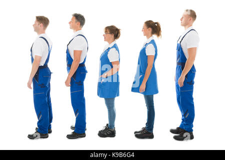 Volle Länge seitliche Ansicht der männlichen und weiblichen Hausmeister stehen in der Warteschlange vor weißem Hintergrund Stockfoto