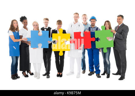 Portrait von selbstbewussten Menschen mit verschiedenen Berufen holding Jigsaw Pieces, während gegen den weißen Hintergrund stehen Stockfoto