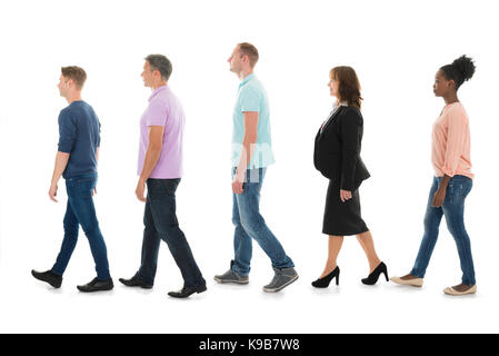 Volle Länge seitliche Ansicht von kreativen Menschen zu Fuß mit Manager in der Zeile vor weißem Hintergrund Stockfoto