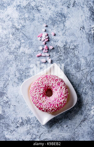 Rosa glasierten Krapfen mit rosa Zucker auf quadratische Platte über grau Textur Hintergrund. Ansicht von oben mit Platz Stockfoto