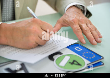 Nahaufnahme eines Geschäftsmannes Füllung Auto Verkauf Vertrag mit Nummernschild auf dem Schreibtisch. Vertrag Papier enthält Platzhalter Text Stockfoto