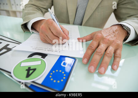 Nahaufnahme eines Geschäftsmannes Füllung Auto Verkauf Vertrag mit Nummernschild auf dem Schreibtisch. Vertrag Papier enthält Platzhalter Text Stockfoto