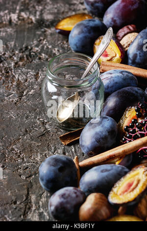 Herbst Pflaumen, Nüssen, Zimt, Glas und Löffel über Braun konkreten Hintergrund. Schließen oben mit Platz für Text. Der herbsternte und Marmelade machen. Stockfoto