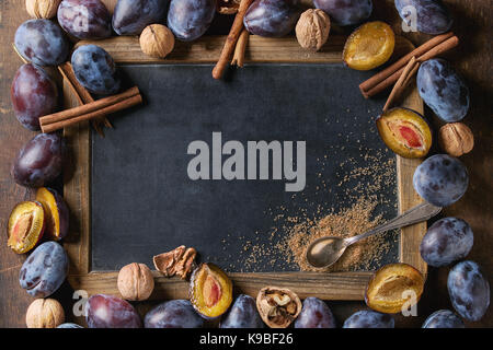 Herbst Rahmen aus Pflaumen, Nüssen, Zimt und Zucker braun mit leeren vintage Tafel über Braun konkreten Hintergrund. Ansicht von oben mit Platz für Text. Fa Stockfoto