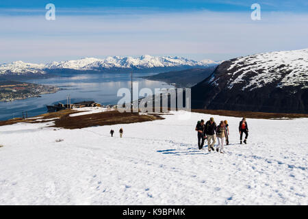 Wanderer zu Fuß durch den Schnee von der oberen Station der Seilbahn Fjellheisen auf dem Berg Storsteinen im Sommer. Tromso, Troms, Norwegen, Skandinavien Stockfoto