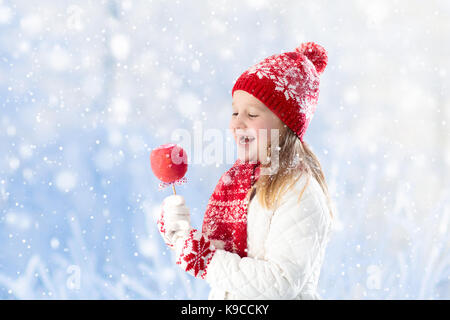 Kind essen Candy Apple im Winter fair. Kinder essen toffee Äpfel auf Weihnachtsmarkt im Schnee. Spaß im Freien auf verschneiter Tag. Familie Urlaub zu Weihnachten Saison. Stockfoto