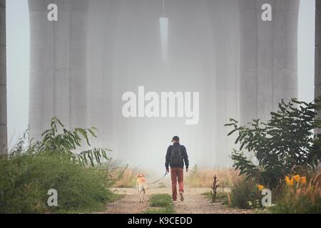 Mann mit Hund unter Autobahnbrücke in den geheimnisvollen Morgennebel. Prag, Tschechische Republik Stockfoto