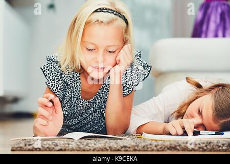 Mädchen liegen auf dem Teppich, ihre Hausaufgaben in der Grundschule. Stockfoto