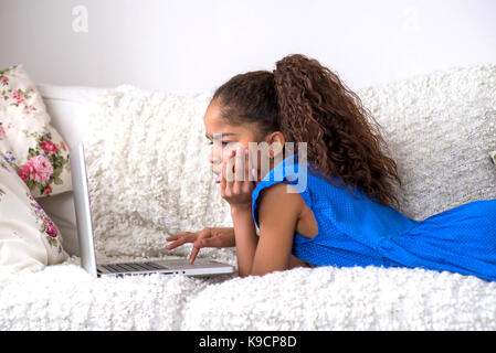 Ein junge schwarze Teenager-Mädchen auf der Couch zu legen und einen Laptop verwenden Stockfoto