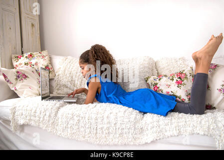 Ein junge schwarze Teenager-Mädchen auf der Couch zu legen und einen Laptop verwenden Stockfoto