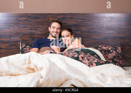Schöne junge Paar vor dem Fernseher im Bett. Stockfoto