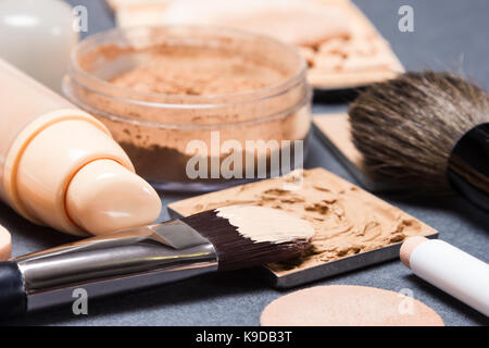 Make-up-Produkte und Zubehör, um sogar aus Hautton und Teint auf Grau texturierte Oberfläche. Seitenansicht, sehr flache Tiefenschärfe Stockfoto