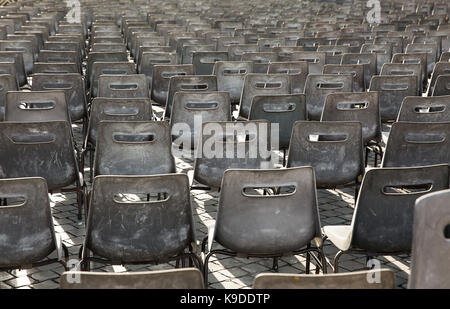 Reihen von leeren grauen Kunststoff Stühle, in einer offenen, sonnigen Platz. Stockfoto