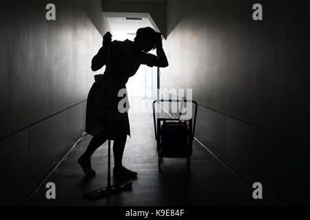 Silhouette von Müde weibliche Maid mit Mop im Korridor Stockfoto