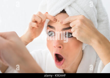 Frau suchen Bei Pickel auf der Stirn im Spiegel Schockiert Stockfoto