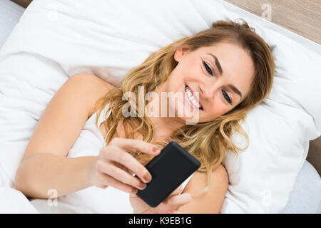 Hohe Betrachtungswinkel und einer Frau liegend auf Bett mit Handy Stockfoto