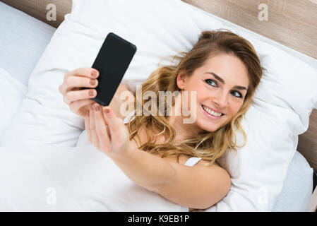 Hohe Betrachtungswinkel und einer Frau liegend auf Bett unter Selfie Stockfoto