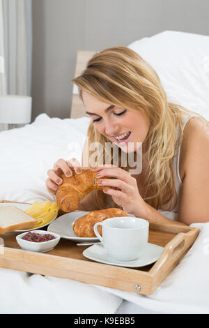 Junge Frau liegend auf Bett mit Frühstück Stockfoto