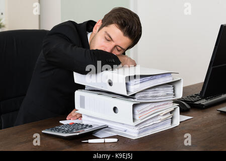 Müde junge Unternehmer Schlafen auf Stapel von Bindemittel am Schreibtisch Stockfoto