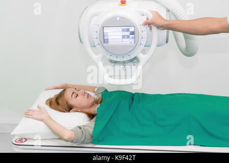 Asiatische junge Frau liegenden Patienten unter X-ray Gerät mit Radiologen Vorbereitung der Maschine in X-ray Zimmer im Krankenhaus. Stockfoto