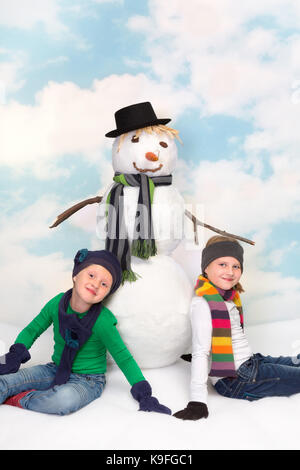 Zwei kleine Schwestern sitzt neben Ihrem neuen Schneemann Stockfoto