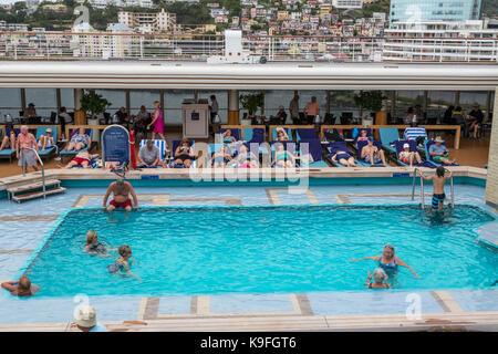 Karibik Kreuzfahrt Schiff Passagiere an Bord Entspannen rund um das Schwimmbad. Fort-de-France, Martinique im Hintergrund. Für die redaktionelle Verwendung. Stockfoto