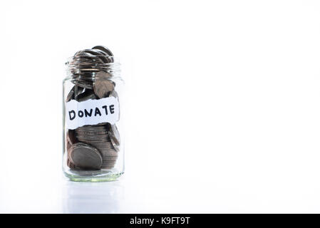 Münzen in Glas Glas mit einer Note geschrieben "Spenden". Auf einem weißen Hintergrund. Geld sparen, um anderen zu helfen. Spendenkonzept und Speichern. M Stockfoto