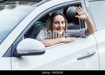 Gut hi! Glück business Frau in einem Auto, in die Kamera schauen und hallo Zeichen senden. Outdoor Foto, Auto- und Sicherheitskonzept Stockfoto