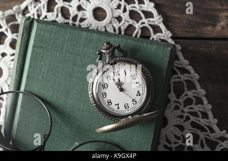 Eine antike Taschenuhr, Gläser und Bücher auf dem Tisch Stockfoto