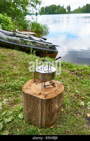 Wandern Herd mit einem Wasserkocher auf einem Baumstumpf und ein Fischerboot auf dem Hintergrund einer See Stockfoto