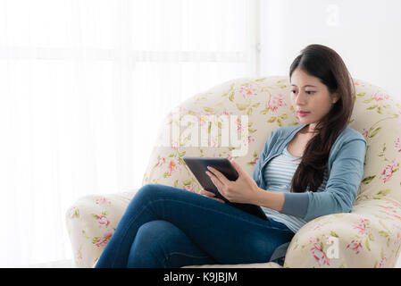 Elegante Schönheit Büro Frau sitzt auf einem Stuhl vor das Fenster ausruhen und mit mobilen digitalen Tablet-e-zu Hause prüfen. Stockfoto