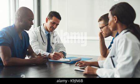 Junge medizinische persönlichen Mitarbeitern treffen einander Sitzen am Tisch im weißen Kittel und blauen Uniform Shirts Stockfoto