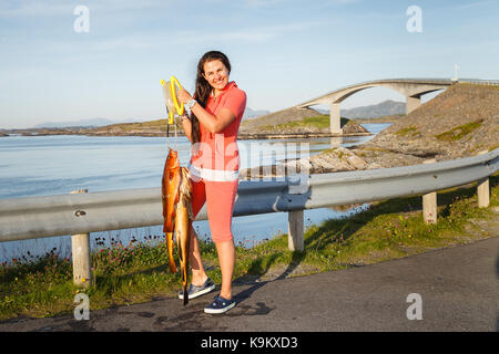 Junge Frau steht auf Atlantik Straße mit frisch gefangenen Norwegische Fische. außenaufnahme in Norwegen. kopieren. Stockfoto