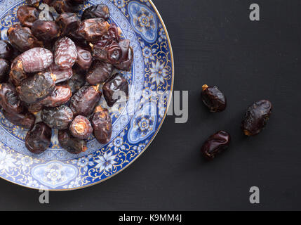 Blick von oben auf die organische bereit Termine in kunstvollen Blau und Gold im Nahen und Mittleren Osten Platte auf rustikalen schwarzer Hintergrund mit Platz für Text zu essen Stockfoto