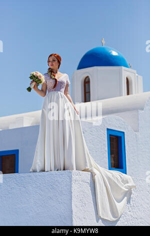 Braut mit einem Strauß Blumen auf der Mauer im Hintergrund der Kirche Stockfoto