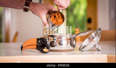 Chili in eine Blechdose geschaufelt wird in eine Metallwanne Stockfoto