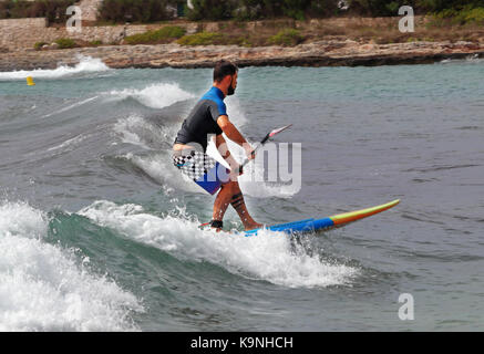 Die Menorquinische Ferienort Punta Prima im Mittelmeer mit männlichen Paddle Board surfen Stockfoto