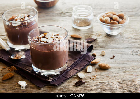 Mousse au Chocolat mit Mandel in Gläsern über Holz- Hintergrund Nahaufnahme - köstliche hausgemachte Raw Vegan Schokoladenpudding mit Nüsse und Johannisbrot- po Stockfoto