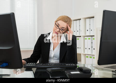 Junge Geschäftsfrau in Kopfschmerzen am Schreibtisch im Büro Stockfoto