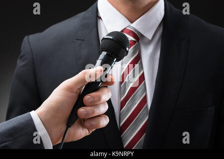 Nahaufnahme einer Hand, die einer Person Mikrofon Vor Geschäftsmann Stockfoto