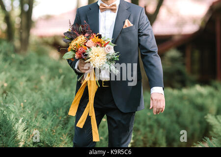 Mode, Herbst, Hochzeit Konzept. jungen gutaussehenden Mann mit Hinreißenden schwarzen Anzug für Verlobte mit weißem Hemd und Fliege, die herrlichen Blumen und gezielt voran gehen Stockfoto